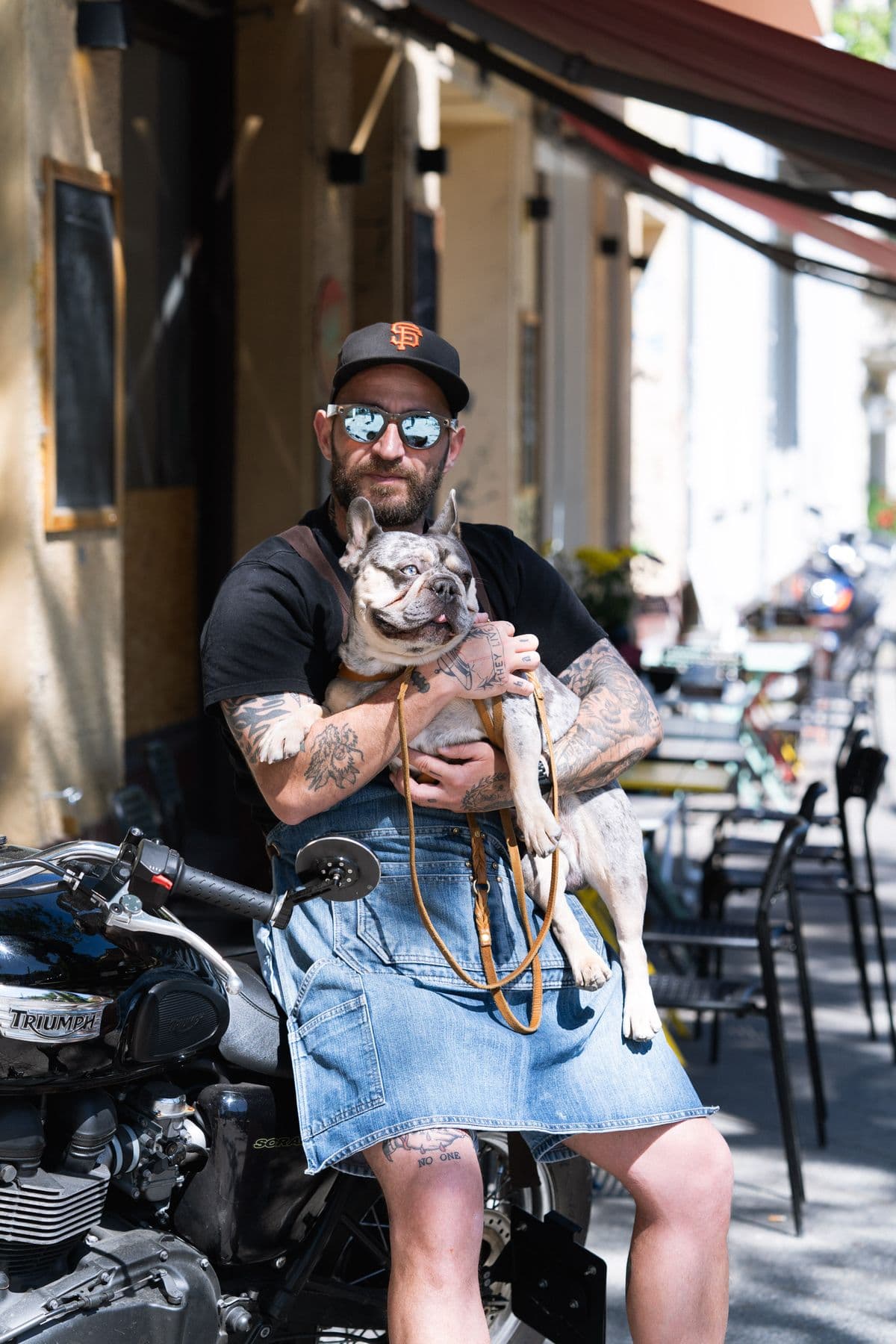 Alessandro mit Cap, Sonnenbrille und Jeansschürze, Fred auf dem Schoß, auf dem Motorrad